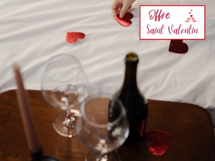 Une bouteille de vin avec deux verres sur une table près d'un lit avec des cœurs découpés